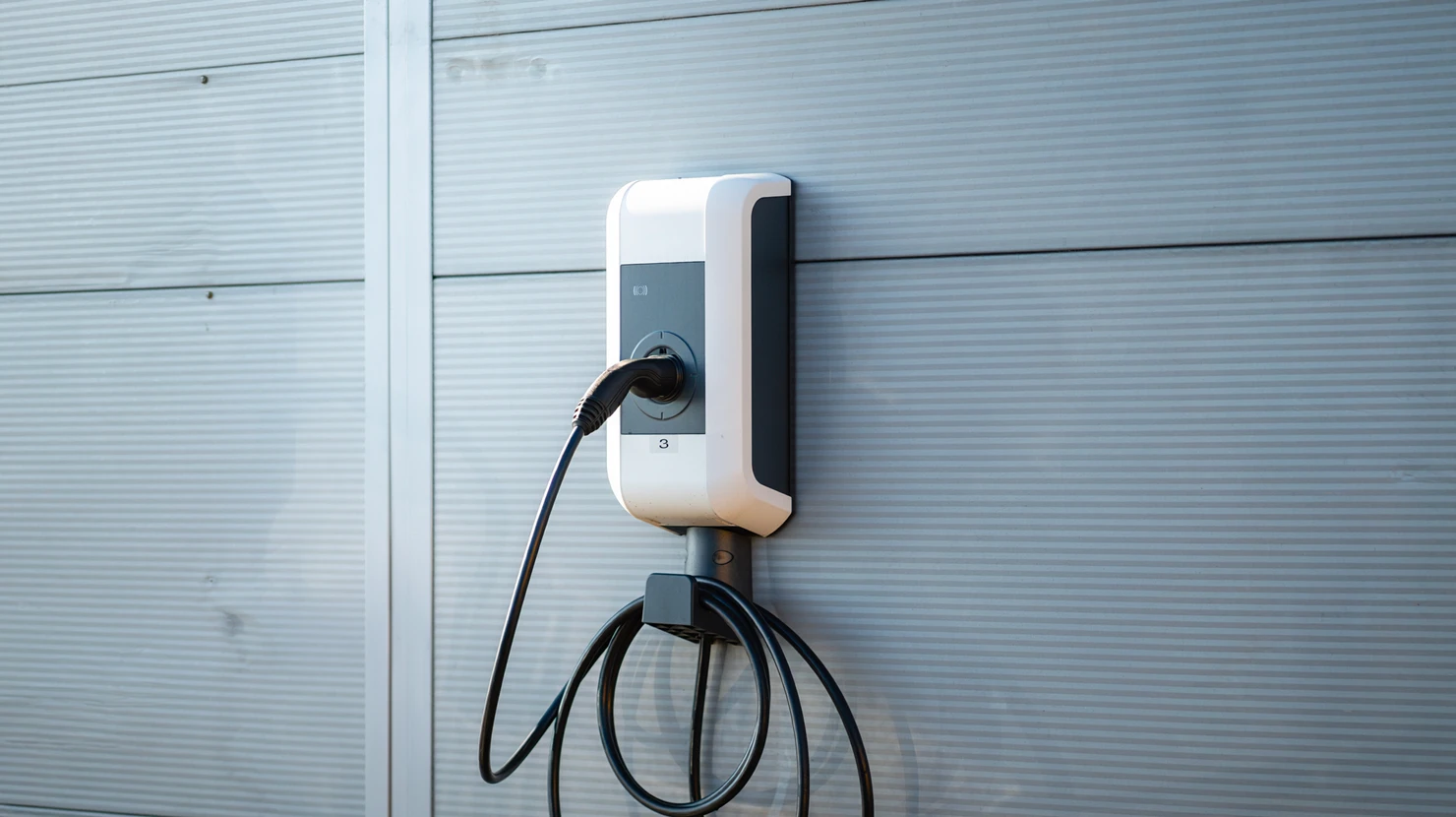 Électricien vérifiant un tableau électrique de distribution avec multiples disjoncteurs modulaires et interrupteurs différentiels, point de vue frontal montrant l'intérieur ouvert de l'armoire avec câblage en conduits et repères visuels, en préparation d'une installation de borne de recharge pour véhicule électrique.