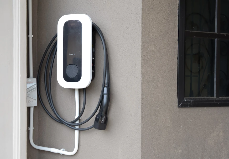 Électricien masculin, barbe courte, installe un luminaire plafonnier sur mur blanc incliné