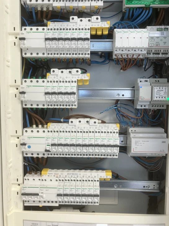 Électricien en t-shirt noir "Gigon Elec" installe un boîtier d'encastrement blanc au plafond d'une salle de bain carrelée
